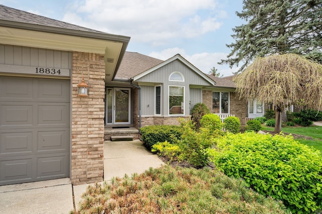 doorway to property with a garage, a shingled roof, and brick siding