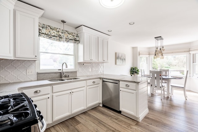 kitchen featuring stainless steel dishwasher, a peninsula, gas range oven, white cabinets, and a sink