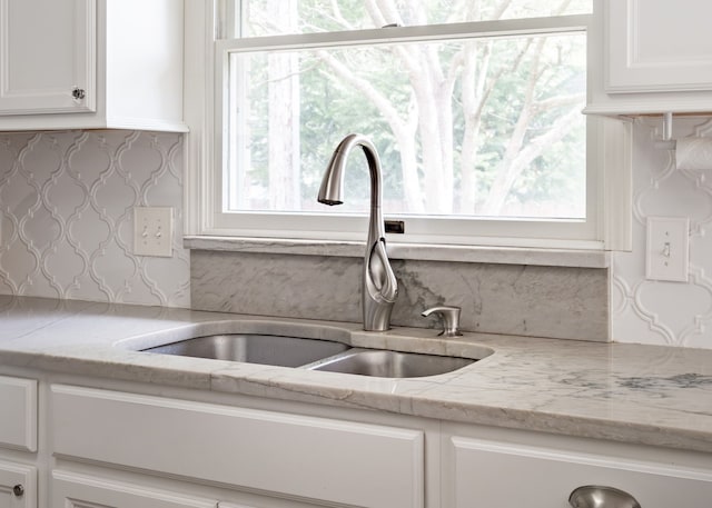 details featuring a sink, white cabinetry, backsplash, and light stone countertops