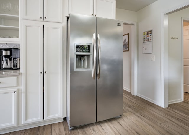 kitchen with light countertops, baseboards, white cabinets, stainless steel fridge, and light wood-style flooring