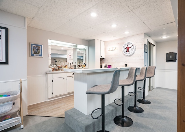 bar featuring wooden walls, a wainscoted wall, indoor wet bar, and a drop ceiling