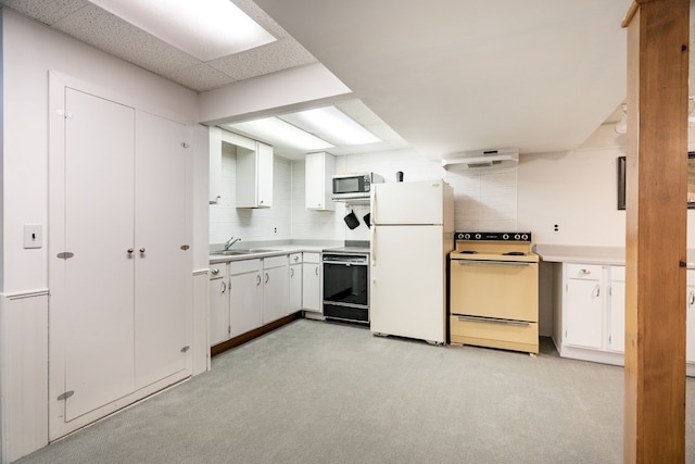 kitchen featuring a sink, light carpet, white appliances, and white cabinetry