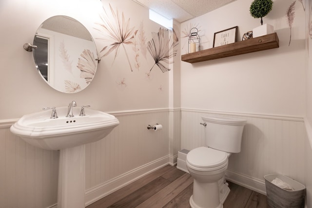 bathroom featuring a wainscoted wall, baseboards, toilet, and wood finished floors