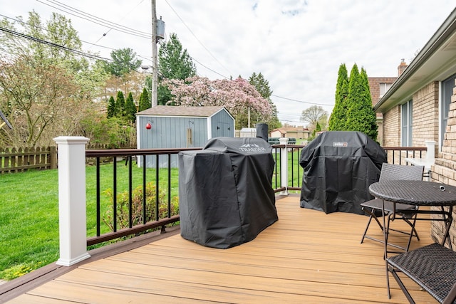 wooden terrace featuring fence, a grill, a yard, a storage shed, and an outbuilding