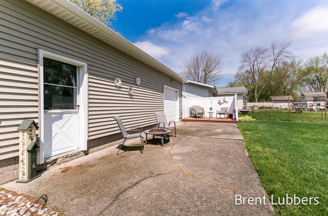 view of patio with an attached garage, an outdoor fire pit, fence, and driveway