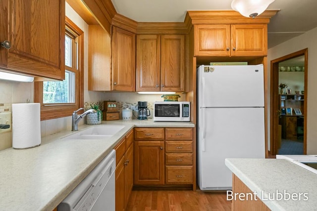kitchen with brown cabinets, a sink, light countertops, light wood finished floors, and white appliances