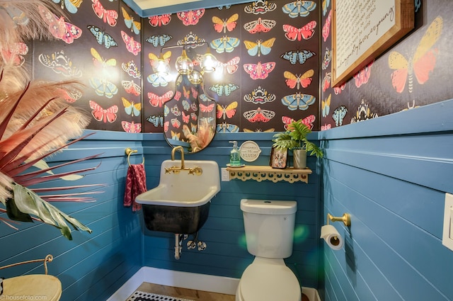 half bathroom with toilet, wallpapered walls, and a sink