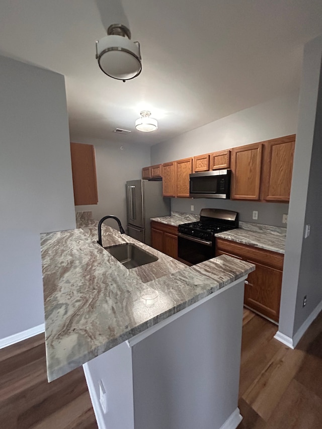 kitchen featuring brown cabinetry, dark wood-style flooring, a sink, a peninsula, and stainless steel appliances
