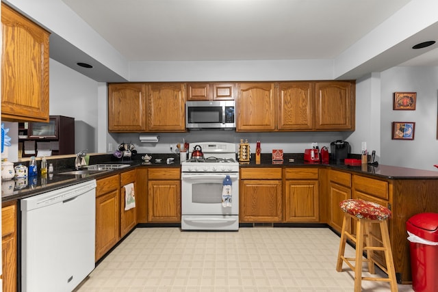 26901 Ann Arbor Trl, Dearborn Heights, MI 48127 - kitchen with white appliances, brown cabinetry, a peninsula, a sink, and dark countertops