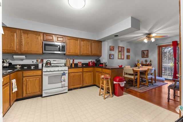 26901 Ann Arbor Trl, Dearborn Heights, MI 48127 - kitchen with stainless steel microwave, white range with gas cooktop, and brown cabinetry