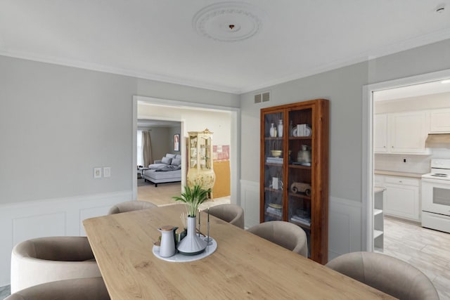 dining area with visible vents, ornamental molding, wainscoting, and a decorative wall