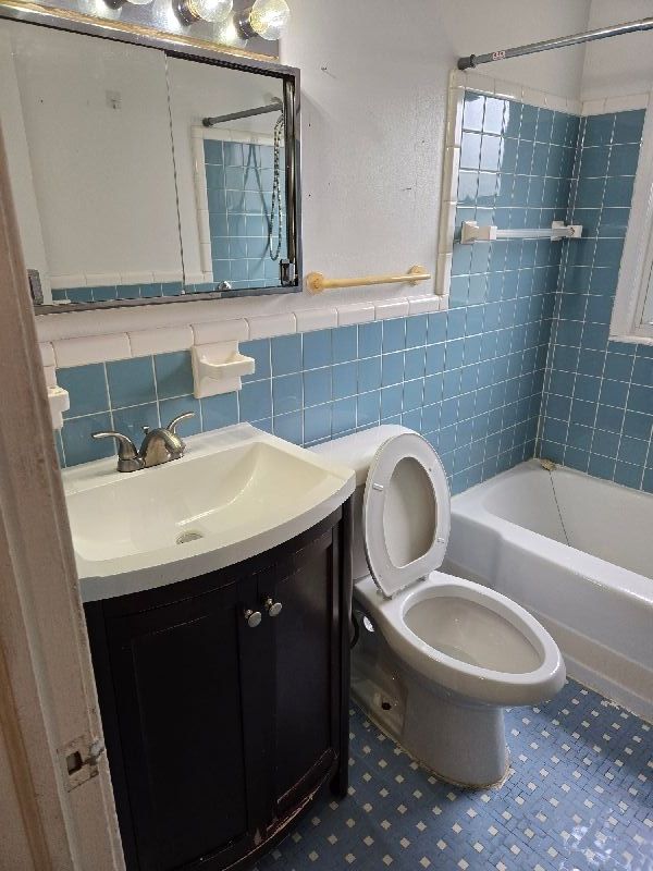 bathroom featuring vanity, toilet, tile walls, shower / tub combination, and a wainscoted wall