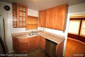kitchen featuring light countertops, brown cabinetry, baseboards, dark wood-type flooring, and stainless steel dishwasher