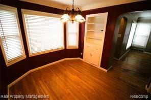 unfurnished dining area featuring arched walkways, an inviting chandelier, dark wood-style floors, and a healthy amount of sunlight