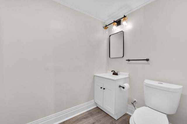 bathroom with toilet, wood finished floors, vanity, baseboards, and ornamental molding