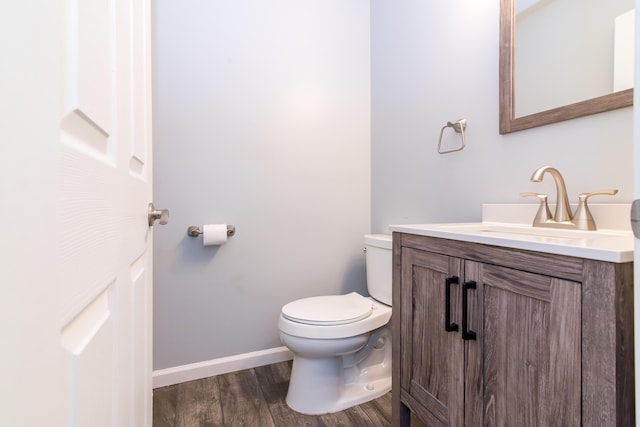 half bath with toilet, baseboards, wood finished floors, and vanity