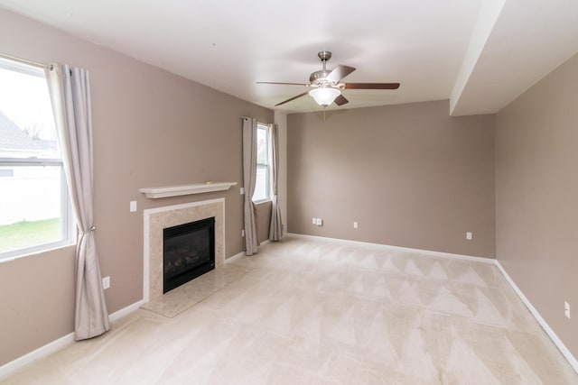 unfurnished living room with baseboards, ceiling fan, a fireplace, and light colored carpet