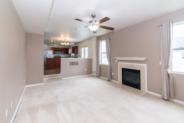 unfurnished living room with light colored carpet, visible vents, ceiling fan with notable chandelier, and a fireplace