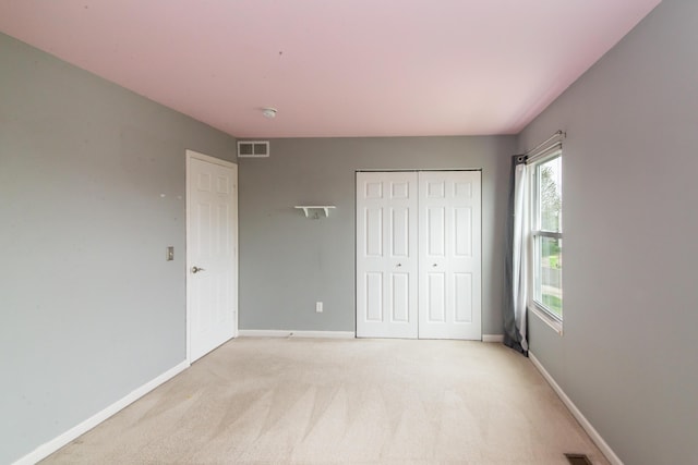 unfurnished bedroom with visible vents, baseboards, a closet, and light colored carpet