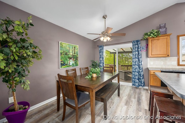 dining space with baseboards, ceiling fan, vaulted ceiling, and light wood-style flooring