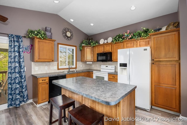 kitchen with vaulted ceiling, plenty of natural light, light wood finished floors, and black appliances