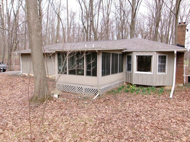 rear view of property featuring roof with shingles, a chimney, and a sunroom