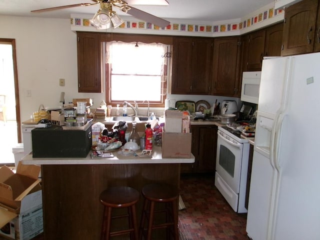 kitchen with white appliances, ceiling fan, a breakfast bar area, light countertops, and brick floor