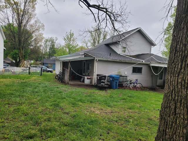 back of property with fence, a yard, and roof with shingles