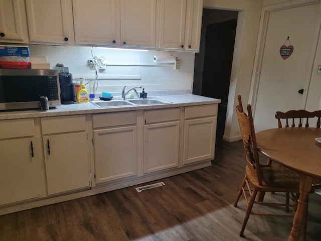 kitchen featuring dark wood-style flooring, visible vents, a sink, stainless steel microwave, and white cabinetry