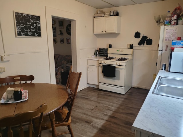 kitchen featuring a sink, white appliances, light countertops, dark wood finished floors, and white cabinetry