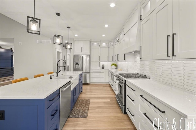 kitchen with a sink, an island with sink, light wood-style flooring, premium appliances, and blue cabinets