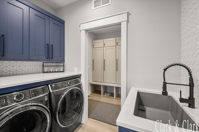 clothes washing area featuring visible vents, washing machine and dryer, a sink, cabinet space, and light wood finished floors
