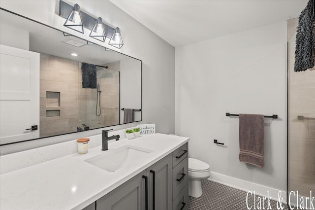 bathroom with vanity, baseboards, tile patterned floors, toilet, and tiled shower