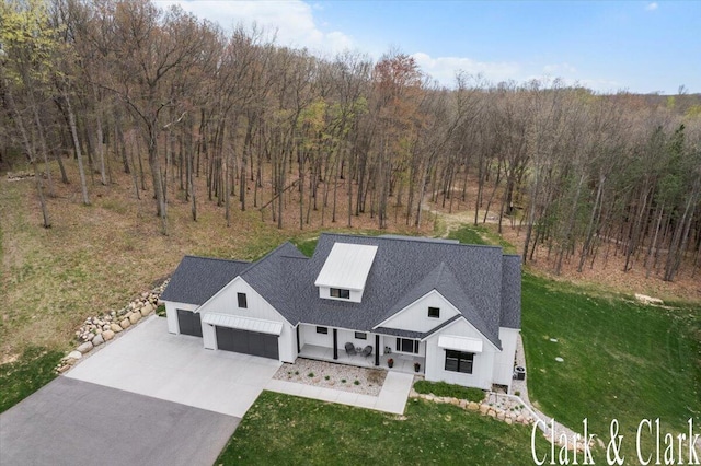 view of front facade featuring a front lawn, board and batten siding, an attached garage, driveway, and a wooded view