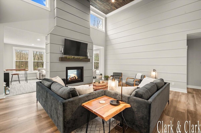 living area with wood walls, a multi sided fireplace, baseboards, wood finished floors, and a towering ceiling