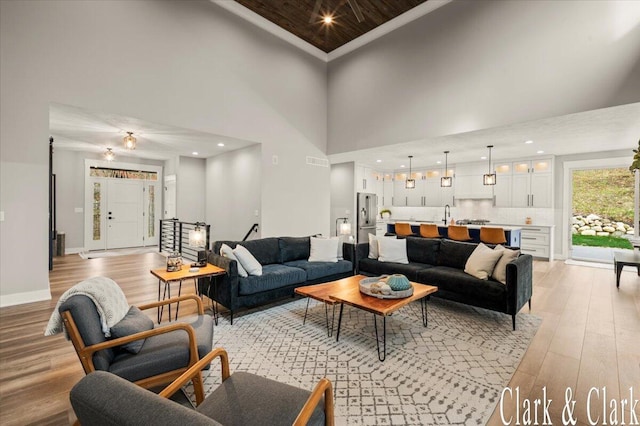 living area featuring crown molding, visible vents, light wood-style flooring, and a towering ceiling
