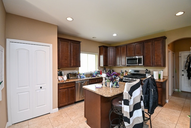12474 Clinton River Rd, Sterling Heights, MI 48313 - kitchen featuring stainless steel appliances, arched walkways, dark brown cabinetry, light stone counters, and light tile patterned floors