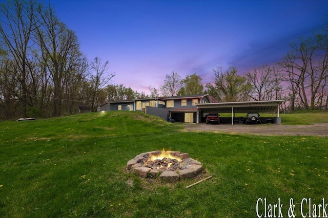 yard at dusk with an outdoor fire pit, dirt driveway, and a carport