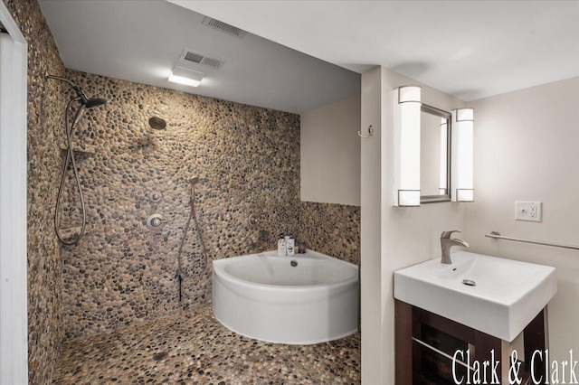 bathroom with visible vents, tiled shower, and vanity