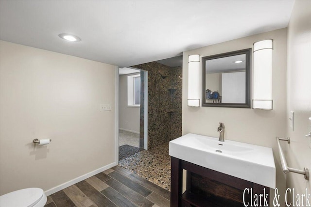 bathroom featuring vanity, wood finished floors, toilet, baseboards, and a walk in shower