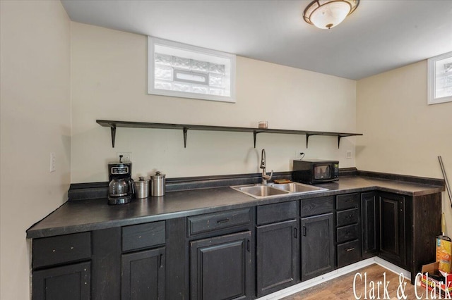 bar with black microwave, a sink, and light wood-type flooring