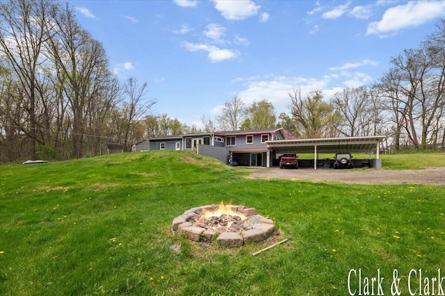 view of yard featuring a carport, driveway, and an outdoor fire pit