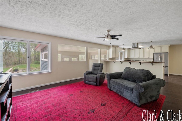 living room featuring a ceiling fan, a textured ceiling, visible vents, dark wood finished floors, and baseboards