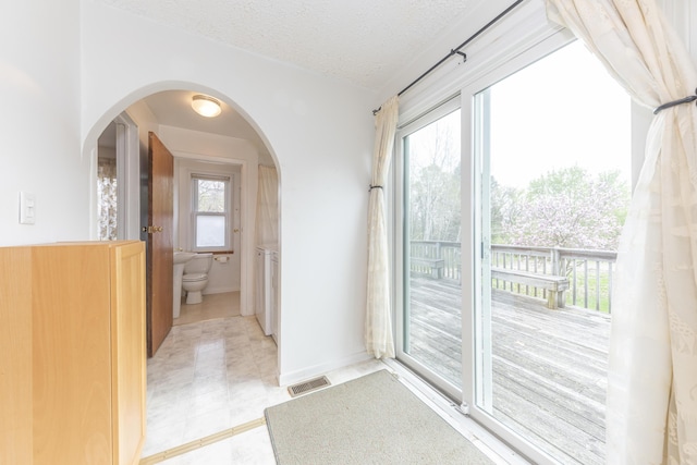 doorway featuring visible vents, a textured ceiling, light tile patterned flooring, and a healthy amount of sunlight
