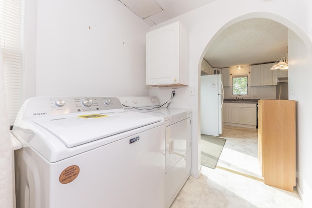 clothes washing area with washer and dryer, cabinet space, a sink, arched walkways, and a textured ceiling