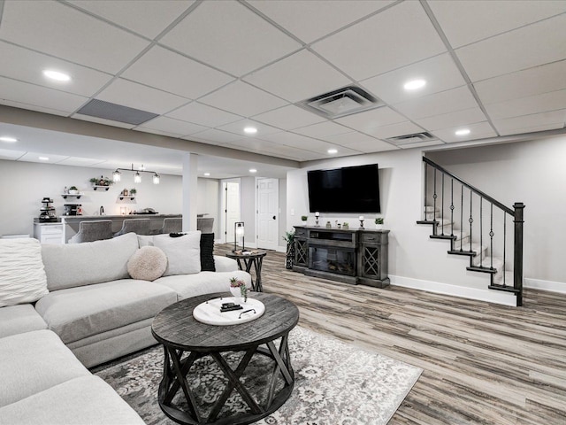living room with wood finished floors, baseboards, stairs, bar area, and a glass covered fireplace