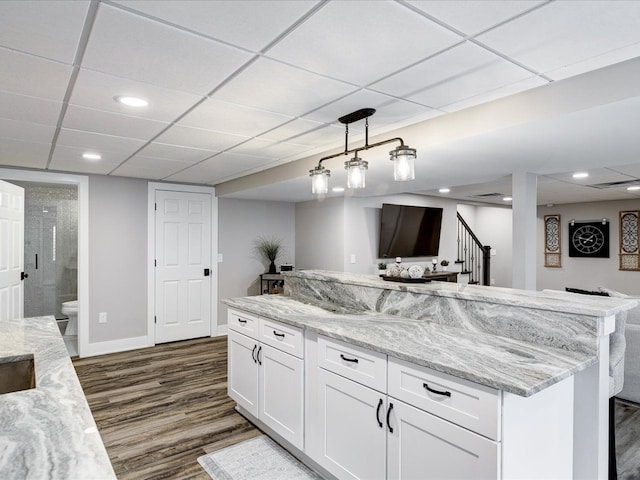 kitchen featuring dark wood-style flooring, white cabinetry, open floor plan, a drop ceiling, and light stone counters