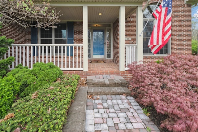 view of exterior entry with brick siding and covered porch