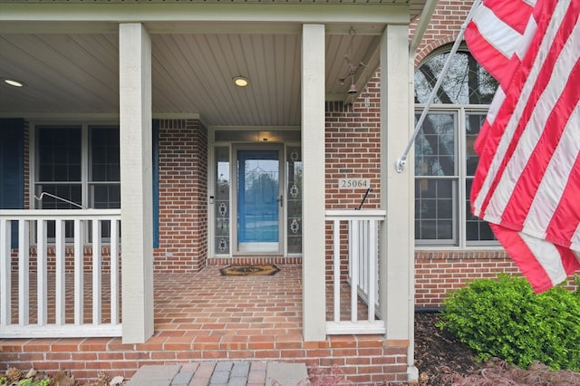 doorway to property with a porch and brick siding