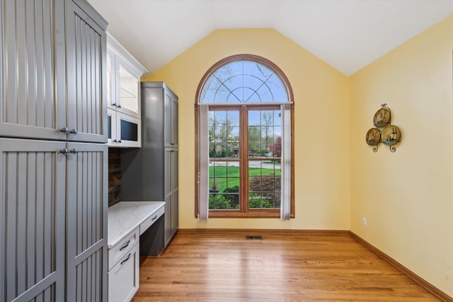 interior space with a wealth of natural light, light wood-style floors, visible vents, and vaulted ceiling